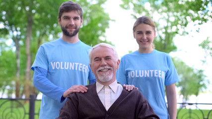 Happy senior man and two volunteers smiling at camera, elderly people support