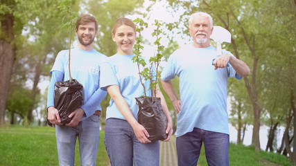 Smiling eco activists holding tree saplings and shovel in hands, reforestation