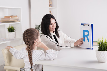 Female therapist working with kid with problem in pronunciation in the white cabinet