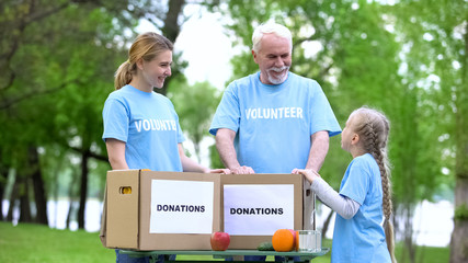 Naklejka premium Child volunteer talking to family, fruits and canned food with donation boxes
