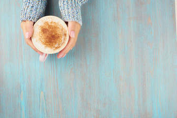 hands holding cup of hot chocolate, blue wooden table, blue cozy sweater, beautiful pink manicure, home style, winter morning, close up, top view, copy space