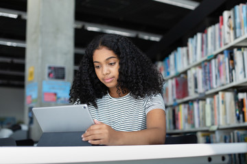 High school african american female student studying with digital tablet in library