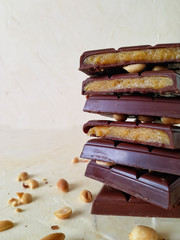 A stack of chocolate pieces stuffed with caramel and peanuts close - up on a light background side view.