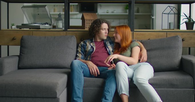 Young couple in love is relaxing on sofa at home, smiling, hugging, celebrating their love, enjoying their relationships, Caucasian. 4K, Middle plan, shot on RED camera.