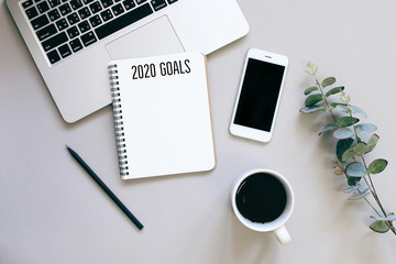 2020 goals on flat lay photo of workspace desk with smartphone, coffee, laptop and notebook with copy space background, minimal style and mockup concept