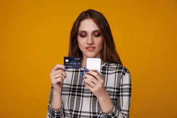 Young woman with phone and credit card standing isolated in the studio