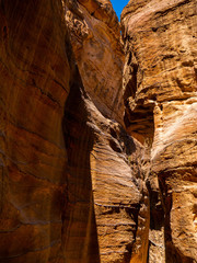 Steep cliffs of a canyon leading to the historical site of Petra, Jordan, light shining from blue sky on dark sandstone walls