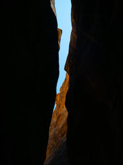Steep cliffs of a canyon leading to the historical site of Petra, Jordan, light shining from blue sky on dark sandstone walls