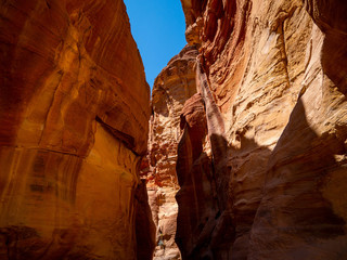 Steep cliffs of a canyon leading to the historical site of Petra, Jordan, light shining from blue sky on dark sandstone walls