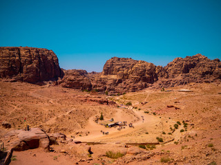 View of the valley of the historic site of Petra, Jordan, orange desert full of temples and a roman amphitheatre, seen from aerial perspective from a sandstone mountain