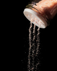 Pink himalayan salt falling out from a salt shaker on a black isolated background
