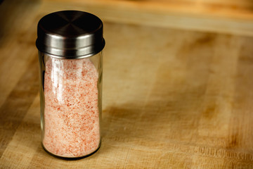 Glass salt shaker with pink Himalayan salt on a wooden chopping board