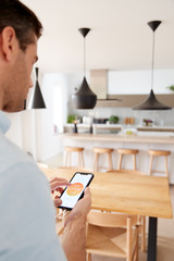 Man Using App On Smart Phone To Control Central Heating Temperature In House
