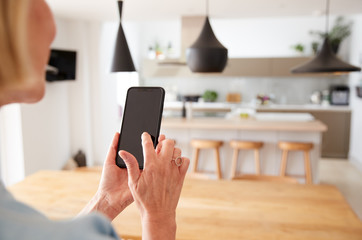 Mature Woman Using App On Mobile Phone To Control Central Heating Temperature In House