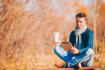 Young man drinking coffee with phone in autumn park outdoors