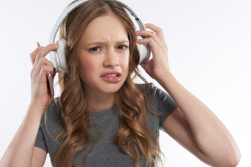 Naklejka premium Displeased teen girl in wireless headphones biting bottom lip