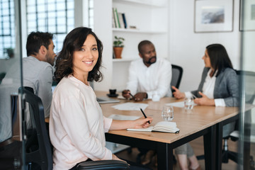 Smiling young businesswoman sitting with coworkers during a meeting