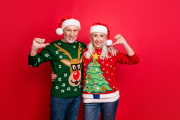Just look at us. Photo of two crazy cheerful delightful confident grey white haired husband wife pointing at themselves showing funky jumpers isolated vivid color background