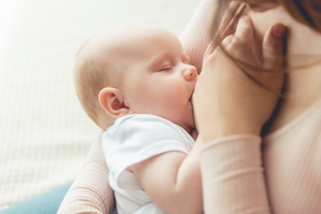 cropped view of mother breastfeeding her child in apartment - obrazy, fototapety, plakaty