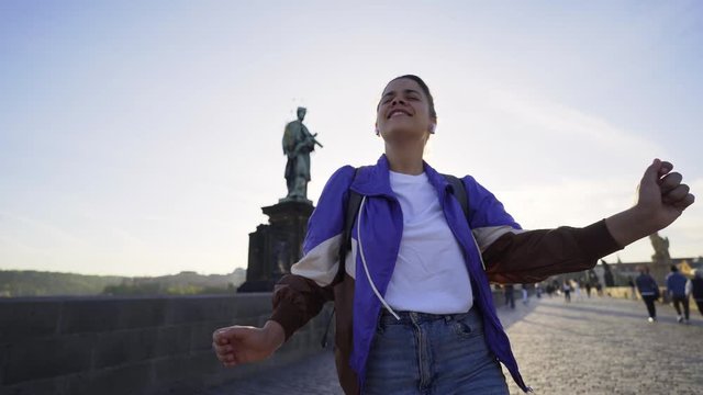 Female walking in historical centre of Prague at morning time. Wide shot woman 80's style clothes have fun, dancing extravagantly. Charming girl fooling around and singing on camera in backlit
