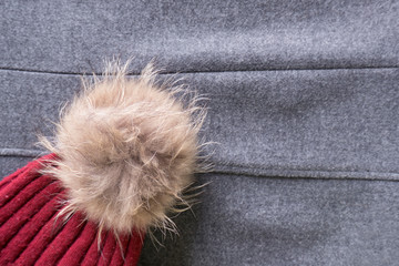 Cozy and warm winter flat lay with copy space. Close up of dark red knitted hat with fur pompom on gray woolen crumpled background
