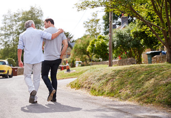 Rear View Of Senior Father With Adult Son Talking As They Walk Along Country Road Together