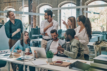 Group of young modern people in smart casual wear communicating and using modern technologies while working in the office