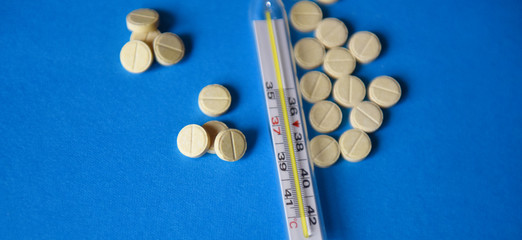 mercury thermometer and pills on blue background