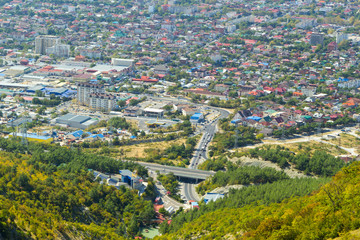 Fototapeta premium Aerial view of Gelendzhik resort city district from hill of caucasian mountains. Buildings and street at the foot of the mountains.
