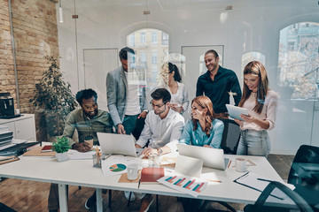 Group of young modern people in smart casual wear communicating and using modern technologies while working in the office