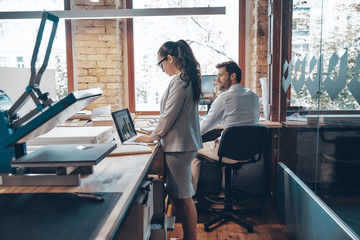 Modern colleagues in smart casual wear communicating and using modern technologies while working in the office