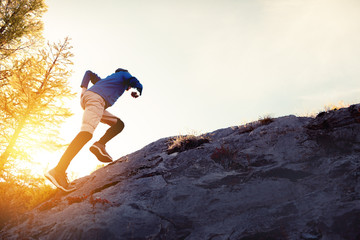 Man runs uphill on big rock at sunset