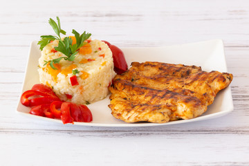 Grilled chicken brest with rice with vegetables and pickles on white plate on white wooden...