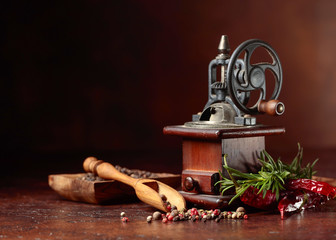 Old pepper mill with cooking utensils,various peppers and rosemary on a brown background.