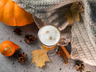 Autumn pumpkin latte glass. A warming drink and a knitted scarf on the gray table. Thanksgiving day