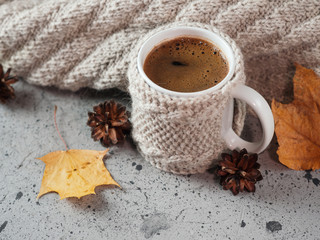 A mug of coffee in a knitted sweater on the table and a knitted wool scarf. Morning Breakfast in cold autumn or winter