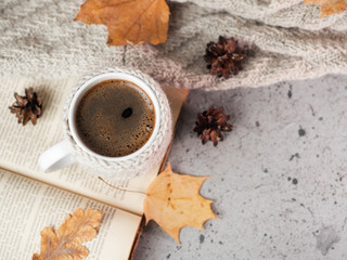 Obraz na płótnie Canvas A mug of coffee in a knitted vest or a handmade sweater and an old book on the table. Autumn composition with a mug of hot coffee and autumn dry leaves. Home comfort. Hygge concept