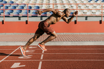 Side view of an athlete starting his sprint on an all-weather running track - obrazy, fototapety, plakaty