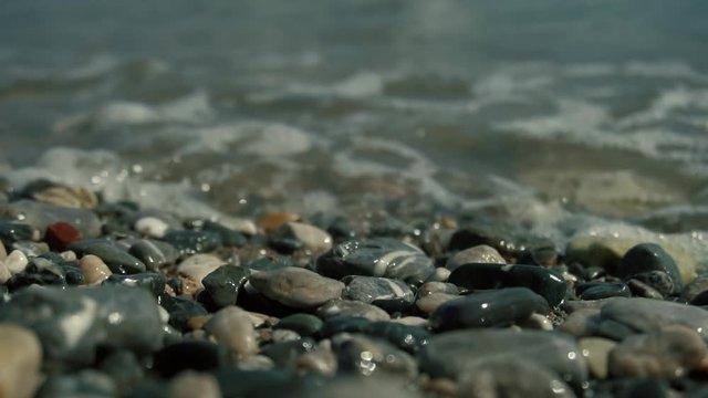 Wave Splashing Over Pebbles At Sea.Vacation Or Summer Holiday Concept.Waves Crashing In Background And Wave Splashing Over Pebbles.Close Up Sea Ocean Beach In Slow Motion.Close-Up Air Buble On Pebbles