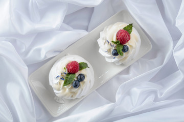 Dessert Pavlova with raspberries, blueberries and mint on a white fabric.