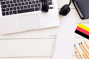 Flat lay frame student desktop with blank spiral notebook, earphones, laptop and German flag. Top view language learning concept
