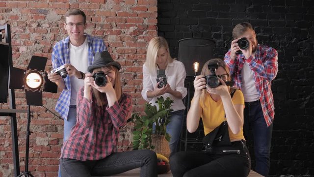 smiling young photographers with different digital cameras in hands take pictures on the background of a brick wall and lamps, masterclass in studio close up