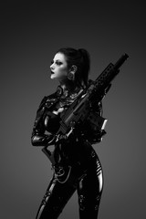 Fototapeta na wymiar Portrait of a young woman in latex jumpsuit holding a machine gun in her hands 