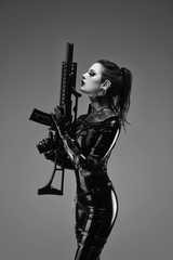 Portrait of a young woman in latex jumpsuit holding a machine gun in her hands	