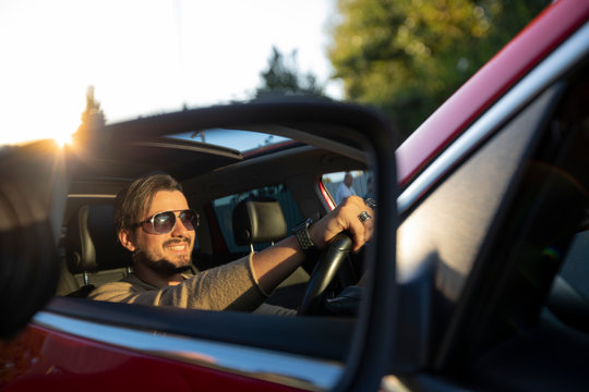 Handsome young man driving a car wihile smiling photographed in the mirror