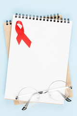 red aids ribbon on open notebook isolated on blue background