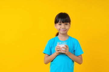 Happy Thai kid holding glass of milk isolated, young Asian girl drinking milk for strong health on yellow background