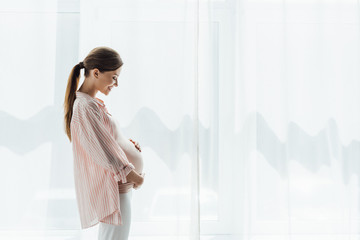side view of happy pregnant woman smiling and touching belly