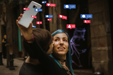 Social media addiction concept: A couple of millenials taking pictures with the smartphone on a street, teenagers lifestyle - obrazy, fototapety, plakaty