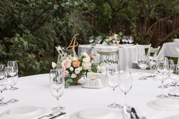 Wedding table setting decorated with fresh flowers in a brass vase. Wedding floristry. Banquet table for guests outdoors with a view of green nature. Bouquet with roses, eustoma and eucalyptus leaves